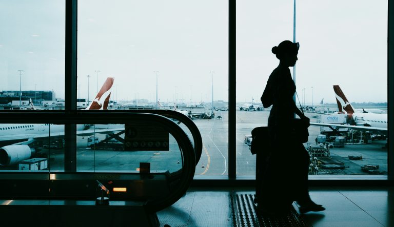 A traveler waits in an airport terminal with aircraft visible through large windows