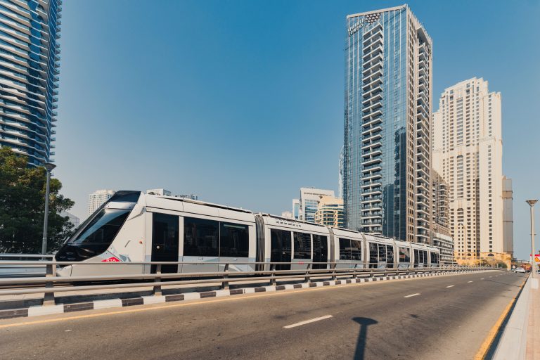 Contemporary tram traversing a road flanked by skyscrapers in Dubai. Urban transportation scene