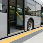 Low-floor bus flush with a raised curb and yellow tactile paving, illustrating level, accessible boarding against a soft city backdrop.