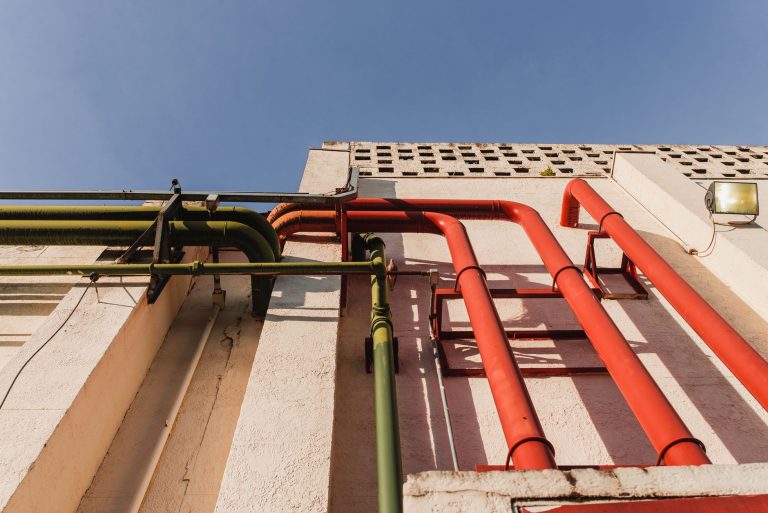 Close-up of vibrant red and green pipes on a sunlit urban building wall