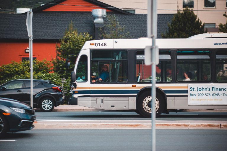 A white public transit bus travelling along an urban street