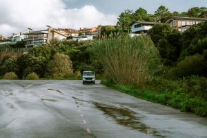 A white van sits on a quiet neighborhood road bordered by trees and homes
