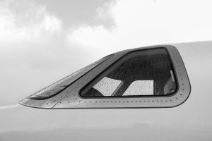Close-up of rain-speckled airplane window in grayscale, showcasing aviation detail